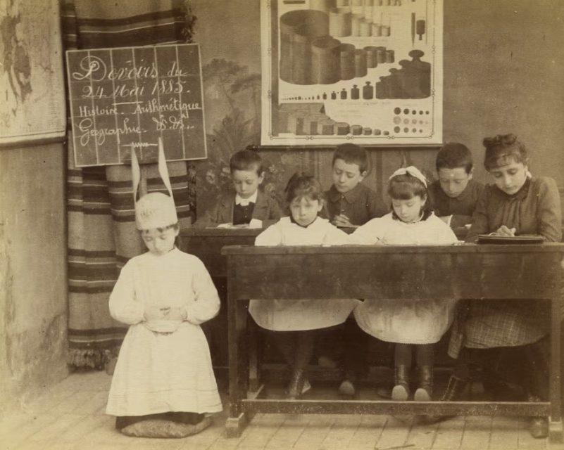 A pupil wearing a dunce’s cap in a French classroom, 24 May 1883.